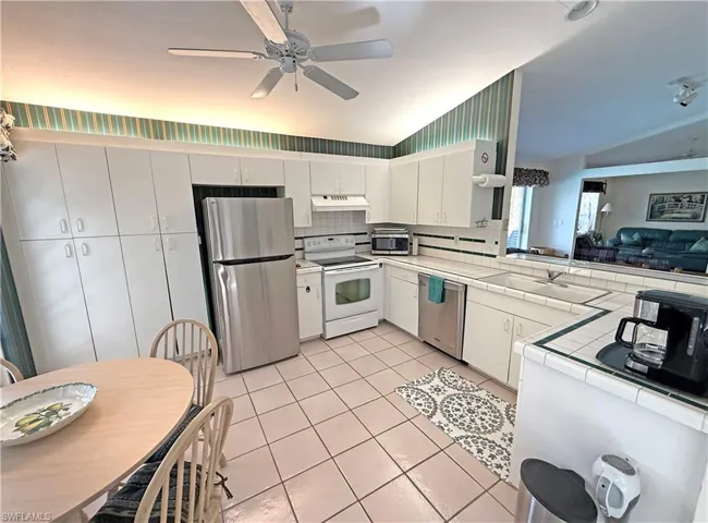 Kitchen with tile counters, backsplash, stainless steel appliances, lofted ceiling, and white cabinetry