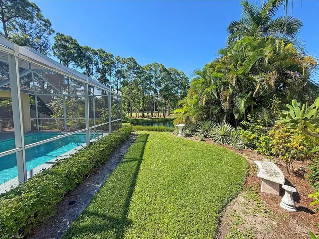 View of grassy yard featuring an outdoor pool, a sunroom, glass enclosure, a water view, and view of scattered trees