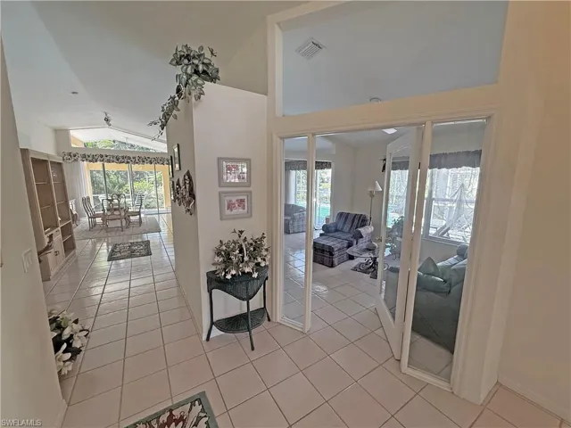 Corridor with light tile patterned floors, high vaulted ceiling, and french doors