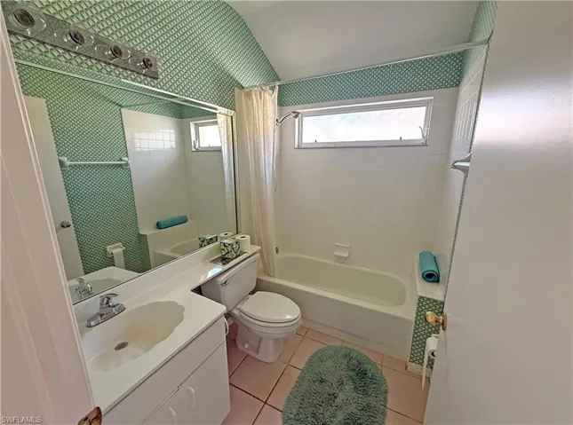 Bathroom featuring light tile patterned floors, shower / tub combo with curtain, vanity, and lofted ceiling