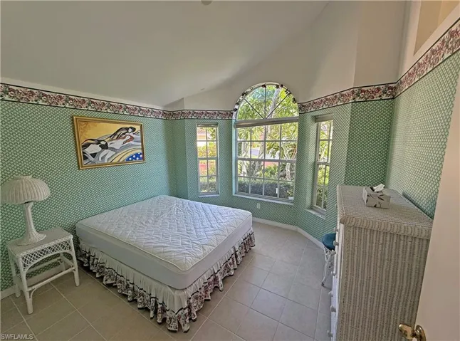 Tiled bedroom featuring lofted ceiling and wallpapered walls