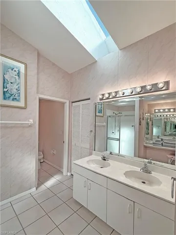 Full bathroom featuring light tile patterned flooring, double vanity, a closet, a skylight, and a stall shower