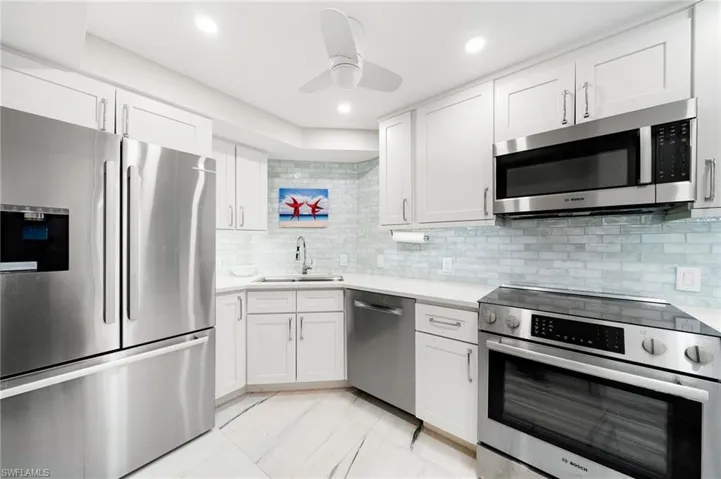 Kitchen featuring decorative backsplash, appliances with stainless steel finishes, sink, and white cabinets
