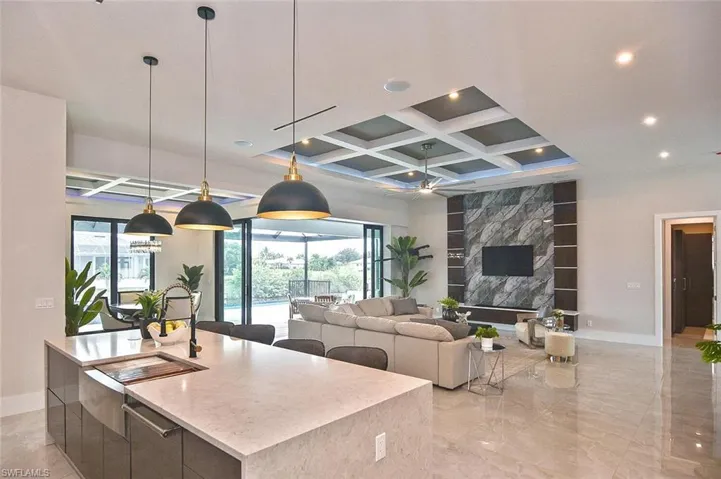 Kitchen featuring hanging light fixtures, modern cabinets, coffered ceiling, healthy amount of natural light, and light stone counters