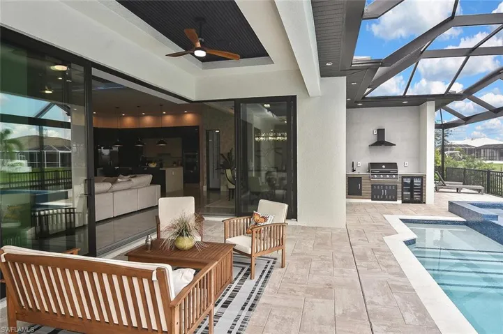 View of patio featuring ceiling fan, an outdoor pool, glass enclosure, a sunroom, and an outdoor kitchen