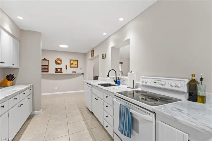 Kitchen with white cabinetry, sink, light tile patterned floors, and white appliances