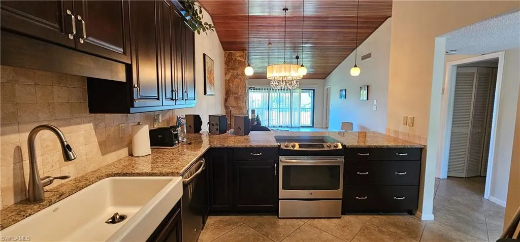 Kitchen featuring kitchen peninsula, appliances with stainless steel finishes, vaulted ceiling, sink, and hanging light fixtures