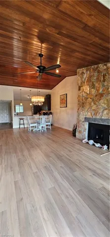 Unfurnished living room featuring a stone fireplace, wood ceiling, ceiling fan with notable chandelier, and light hardwood / wood-style floors