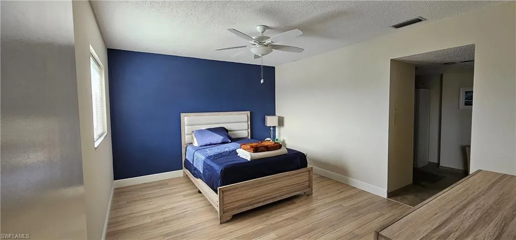 Bedroom with ceiling fan, light wood-type flooring, and a textured ceiling