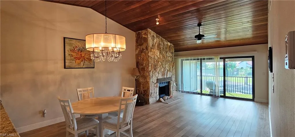 Dining room with high vaulted ceiling, ceiling fan with notable chandelier, a stone fireplace, wood-type flooring, and wood ceiling