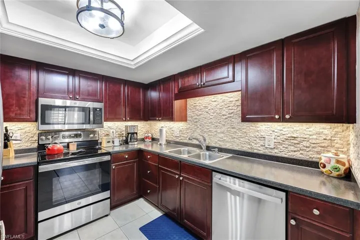 The kitchen features dark cherry cabinetry, stainless steel appliances, and a striking backsplash, creating a sleek and modern aesthetic.