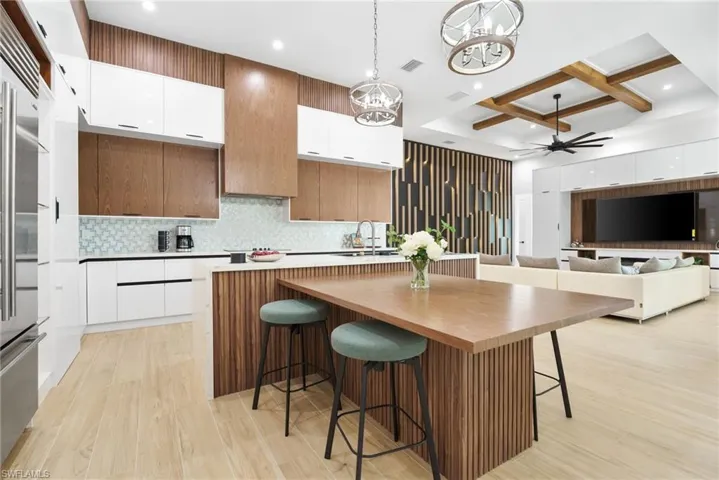 Stunning chef’s kitchen featuring quartz waterfall countertops, dual-toned white and walnut cabinetry, stunning wood paneling accents, high-end appliances, and a hidden butler’s pantry