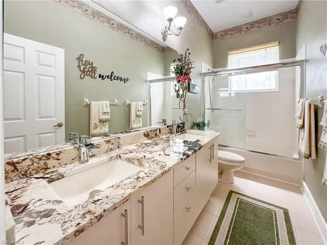 Bathroom with double vanity, bath / shower combo with glass door, and light tile patterned floors