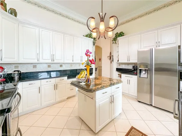 Kitchen with arched walkways, white cabinetry, stainless steel appliances, tasteful backsplash, and dark stone counters