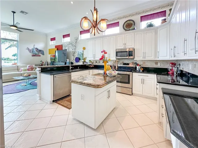 Kitchen with a peninsula, stainless steel appliances, white cabinetry, light tile patterned flooring, and ornamental molding