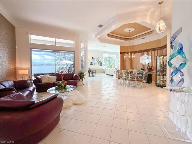 Living room with crown molding, light tile patterned floors, a chandelier, a raised ceiling, and a water view