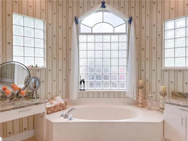 Bathroom featuring wallpapered walls, vanity, and a garden tub