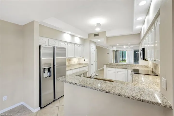 Kitchen featuring a peninsula, appliances with stainless steel finishes, white cabinetry, light stone countertops, and light tile patterned floors
