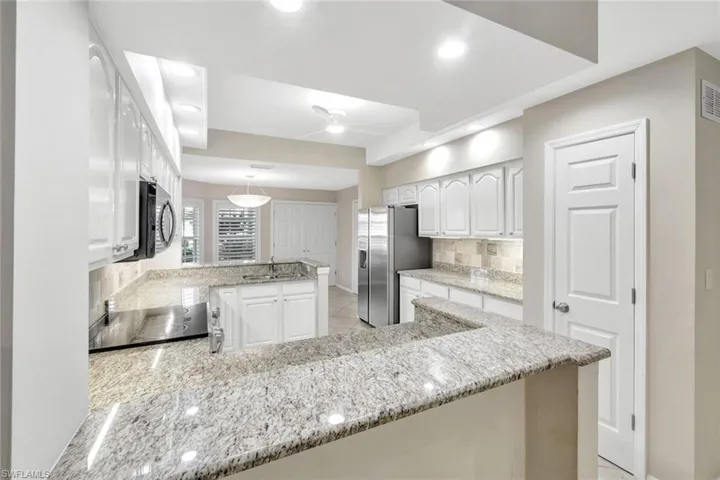 Kitchen with decorative backsplash, light stone countertops, white cabinets, black appliances, and a peninsula