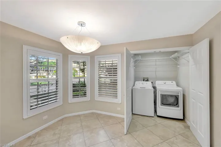 Washroom with washing machine and clothes dryer and light tile patterned flooring