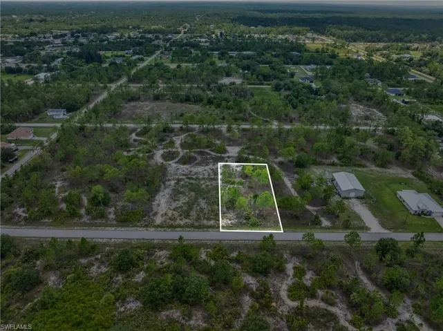 Vacant land parcel featuring mature trees, a clear road frontage, and surrounding undeveloped acreage