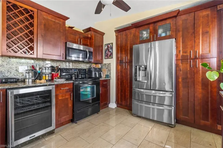 Kitchen with dark stone countertops, wine cooler, decorative backsplash, stainless steel appliances, and reddish brown cabinets