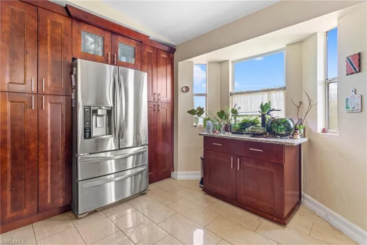 Kitchen featuring stainless steel fridge with ice dispenser, glass insert cabinets, baseboards, dark brown cabinets, and light stone countertops