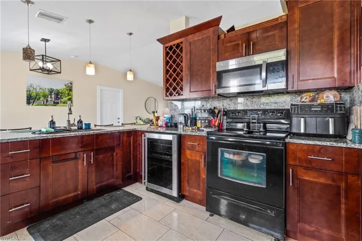Kitchen with visible vents, stainless steel microwave, a sink, black range with electric cooktop, and wine cooler