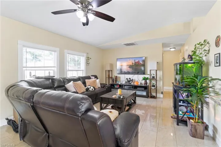 Living room with lofted ceiling, visible vents, baseboards, and ceiling fan