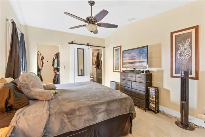 Bedroom with baseboards, a spacious closet, a ceiling fan, a barn door, and visible vents