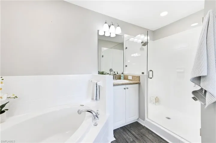 Full bathroom with vanity, a bath, a stall shower, and dark wood-type flooring
