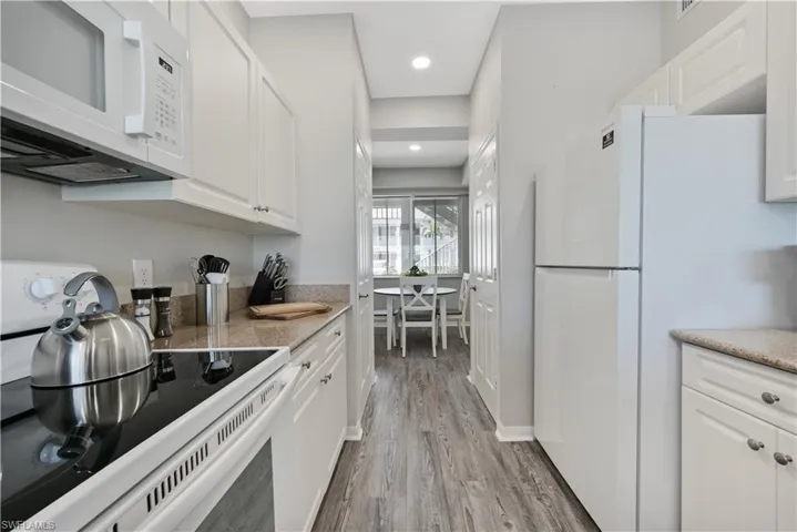 Kitchen featuring white appliances, white cabinets, light wood finished floors, light stone counters, and recessed lighting