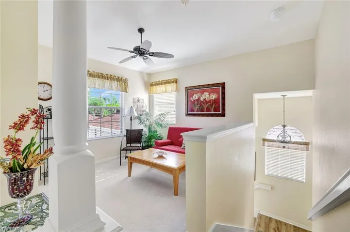 Living area featuring ornate columns, light carpet, and a ceiling fan