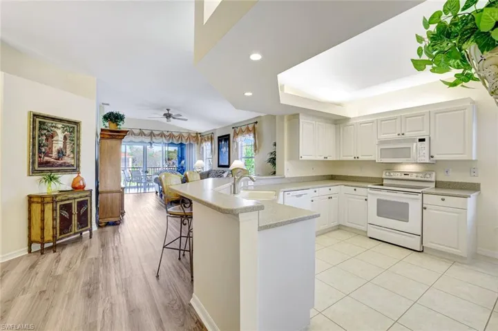 Kitchen with a peninsula, white appliances, a breakfast bar, ceiling fan, and white cabinets