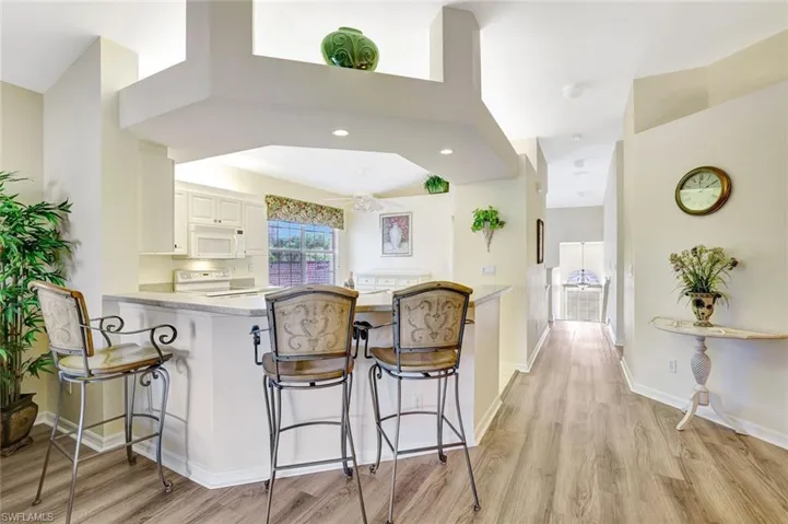 Kitchen featuring a breakfast bar area, white cabinets, white appliances, light wood-style flooring, and a peninsula