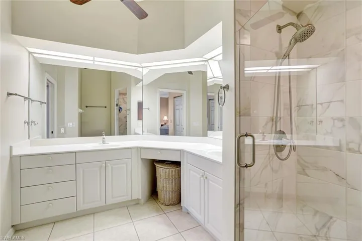 Full bath featuring a marble finish shower, double vanity, ceiling fan, and light tile patterned floors