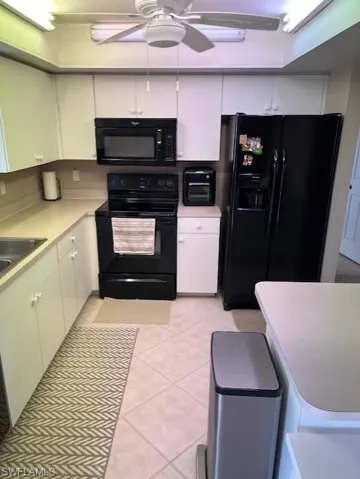 Kitchen with black appliances, white cabinets, and light tile patterned flooring