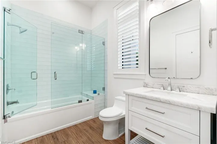 Full bathroom featuring vanity, shower / bath combination with glass door, toilet, and hardwood / wood-style flooring