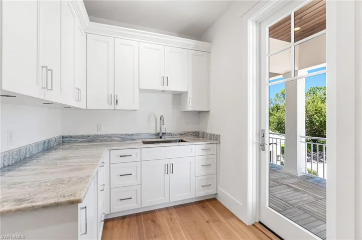 Kitchen with white cabinets, light wood-type flooring, light stone countertops, and sink