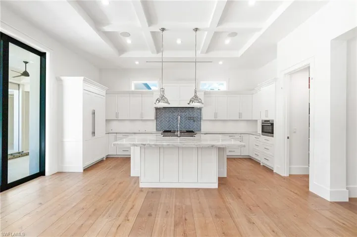 Kitchen featuring decorative backsplash, light hardwood / wood-style flooring, coffered ceiling, and an island with sink