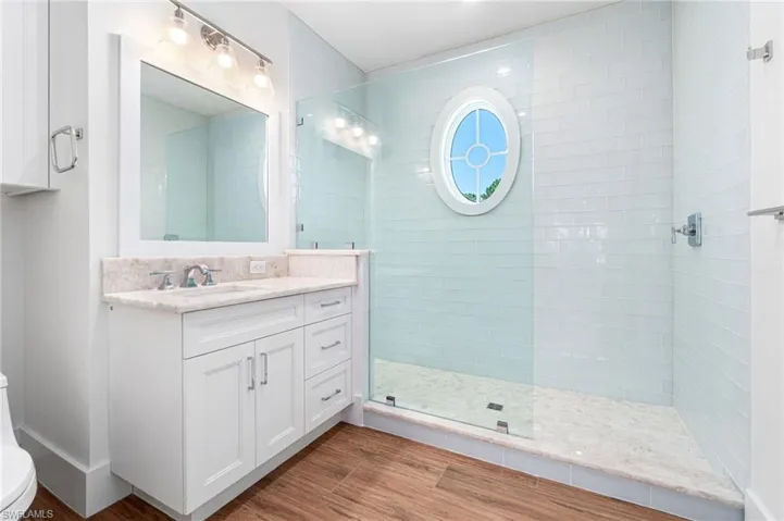 Bathroom with hardwood / wood-style flooring, a shower with door, toilet, and vanity