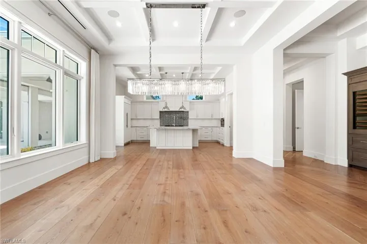 Unfurnished living room with beam ceiling, light hardwood / wood-style floors, a notable chandelier, and coffered ceiling