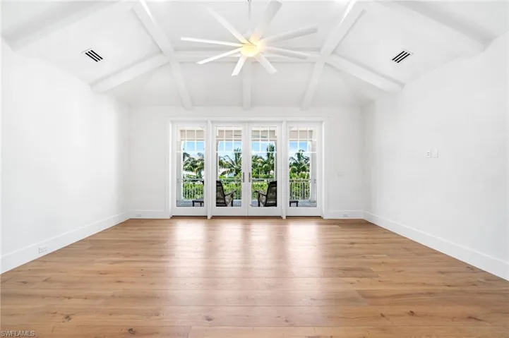 Empty room featuring lofted ceiling with beams, ceiling fan, light wood-type flooring, and french doors