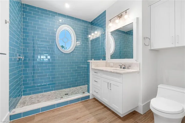 Bathroom with a shower with shower door, vanity, wood-type flooring, and toilet