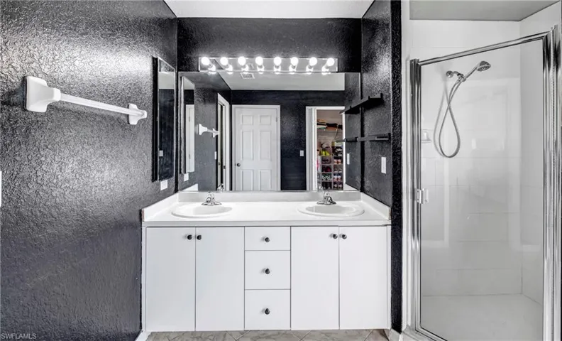 Bathroom featuring a textured wall, double vanity, and a shower stall