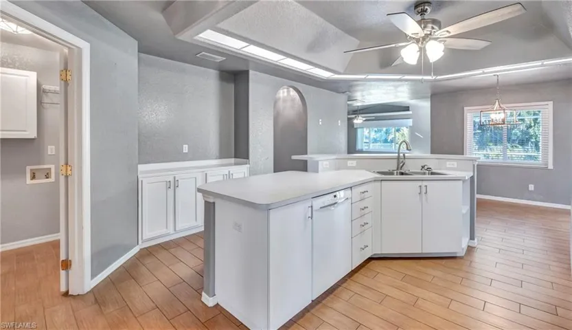 Kitchen with white cabinets, light countertops, wood finish floors, a ceiling fan, and an island with sink