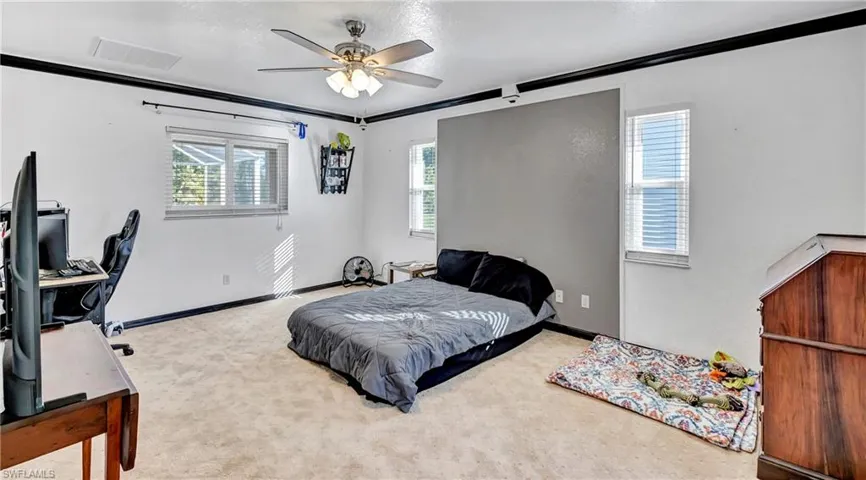 Carpeted bedroom with ceiling fan and crown molding