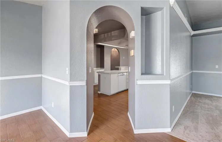 Corridor with a textured wall, light wood-type flooring, and arched walkways