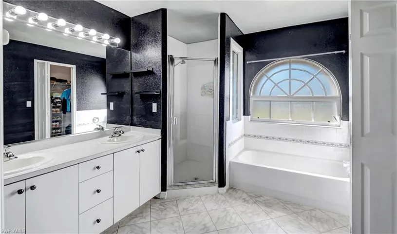 Full bathroom with a shower stall, a bath, double vanity, and a walk in closet