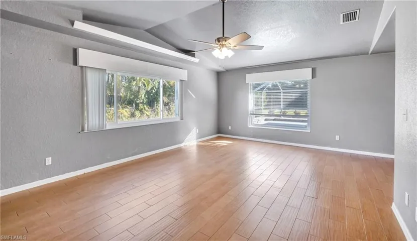 Spare room with a textured wall, lofted ceiling, light wood-style flooring, a ceiling fan, and plenty of natural light